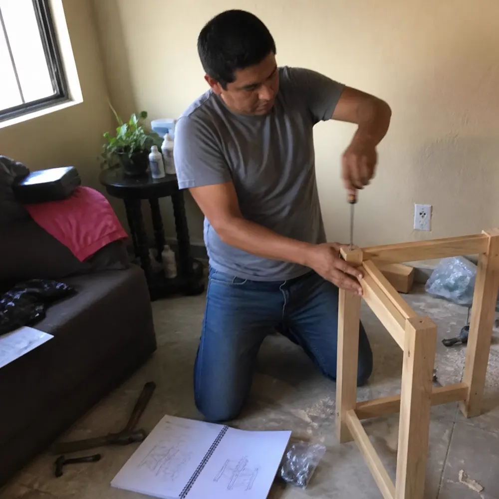 Persona armando una silla de madera en su casa siguiendo el manual impreso