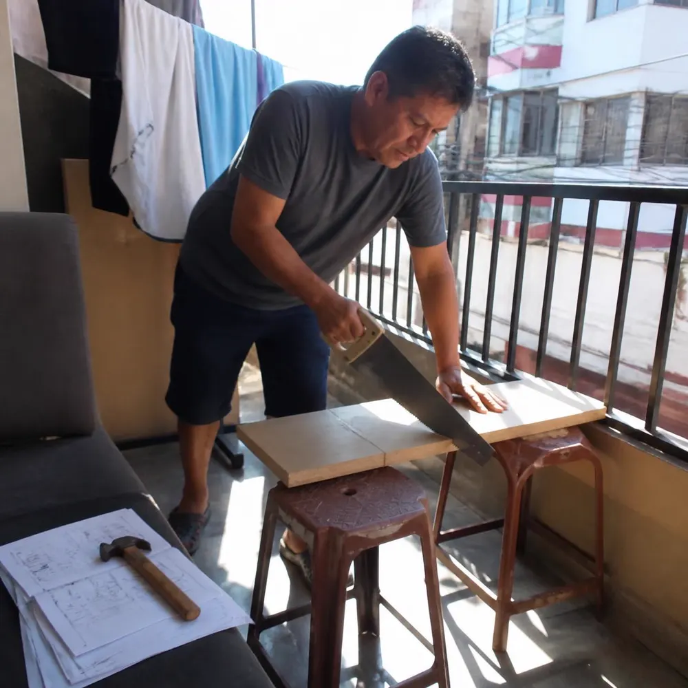 Hombre cortando una tabla de madera en el balcón de su departamento